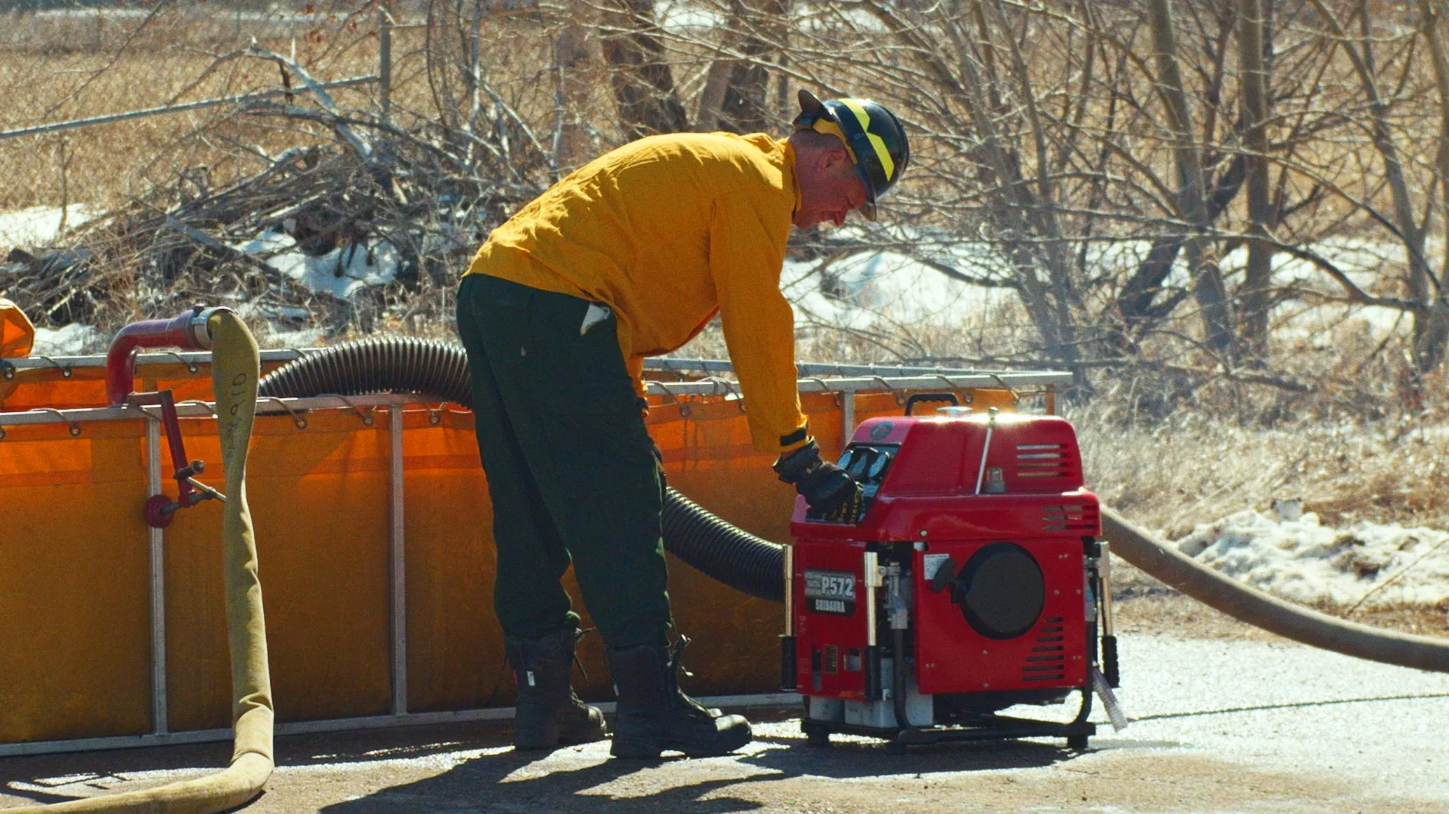 Firefighter operating a portable fire pump beside a remote water tank