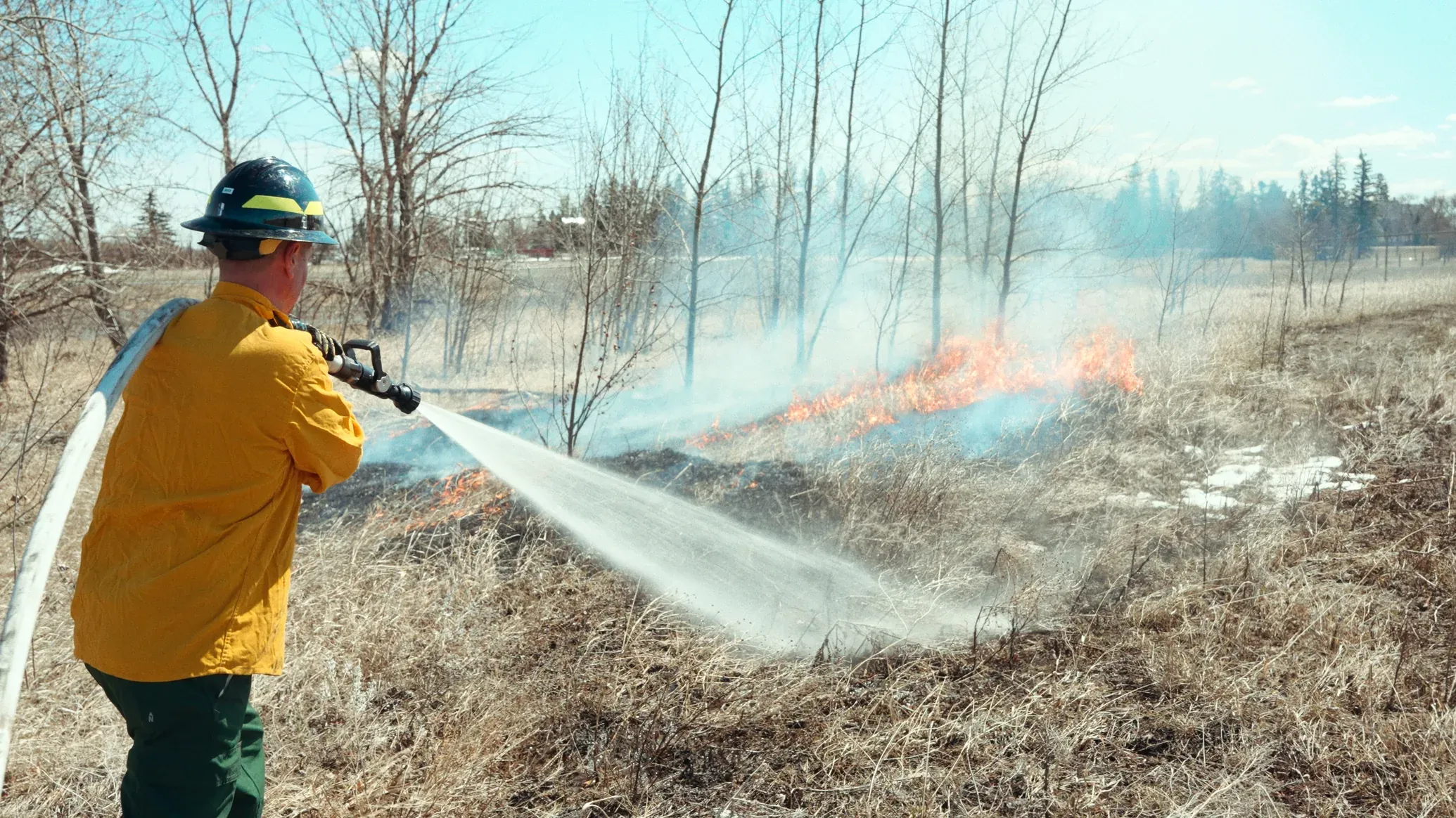 Firefighter using a portable fire pump to spray water on a grass fire